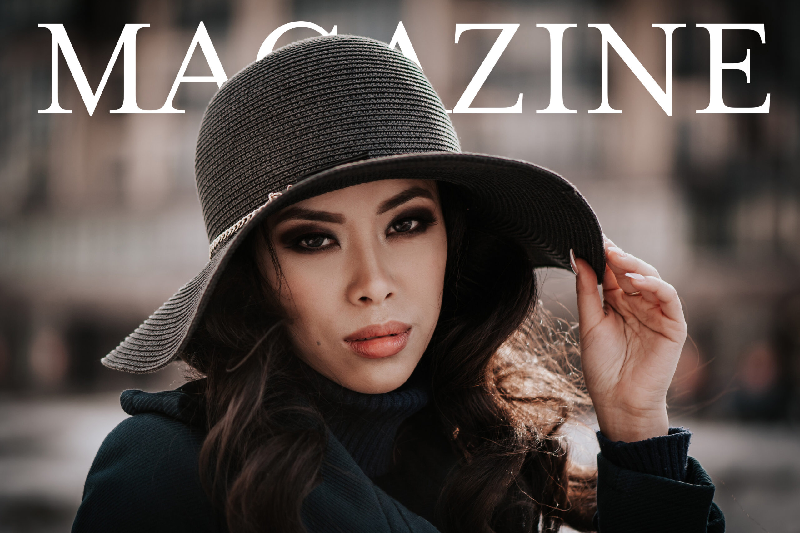 A woman looking straight ahead in a black coat and large-brimmed black sun hat, hand resting on the brim, with the word 'Magazine' partially obscured by her head.